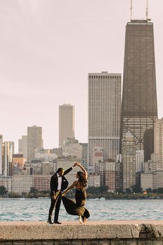 a man and woman dancing by the water in front of a cityscape with skyscrapers