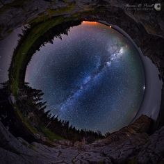 the night sky is reflected in a round hole with trees and rocks around it,