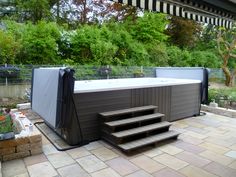 an outdoor hot tub sitting on top of a patio next to a tree and bushes