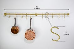 two copper pots hanging from hooks on a white wall next to a measuring line with measurements