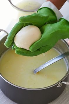 a person wearing green gloves is washing an egg in a pan