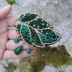 a person holding a green brooch with beads and stones on it's side