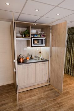 a kitchen with wooden floors and white walls, has a microwave on the cabinet door