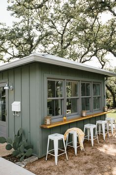 an outdoor bar with stools and tables in front of it, next to trees