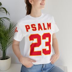 Elevate your game on and off the field with our Psalm 23 football jersey T-shirt. This unique jersey combines your love for football with the inspirational words of Psalm 23. Crafted for both performance and style, it's perfect for sports enthusiasts who seek strength and guidance in their faith. Made from high-quality materials and featuring a bold, eye-catching design, this shirt will have you feeling empowered and focused. Show your faith and passion for the game with this one-of-a-kind footb White Jersey T-shirt For Football Season, Collegiate White Tops With Number Print, Collegiate White Top With Number Print, Football Season Fan Apparel Jersey With Short Sleeves, Sporty Number Print Tops For Fan Gear, White Number Print T-shirt For College, Team Spirit Top With Number Print, Football Season Short Sleeve Letter Print Jersey, Football Season Letter Print Short Sleeve Jersey