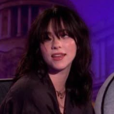 a close up of a person sitting in a chair with a purple light behind her