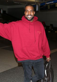 a man in a red hoodie is holding his hand out to the side while walking through an airport