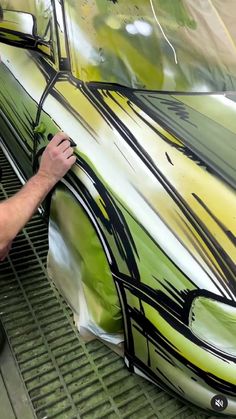 a man is painting a car on the side of a building with green and yellow paint