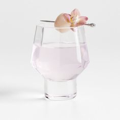 a flower in a glass filled with water on a white surface, next to a spoon