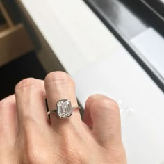 a person's hand holding an engagement ring with a diamond in the middle and a window behind it