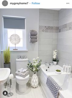 a white bathroom with gray and white decor on the walls, toilet, tub, sink and window