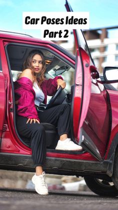 a woman sitting in the driver's seat of a red car with the door open