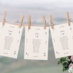 wedding seating cards hanging from clothesline with flowers and greenery in the foreground