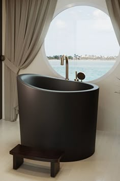 a round window with curtains and a black bathtub in front of the tub is next to a wooden bench