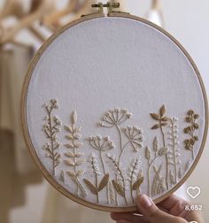 a person holding up a white embroidery hoop with flowers on the front and back side