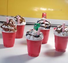 six red cups filled with ice cream covered in chocolate and sprinkles,