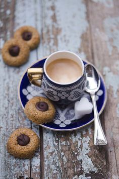 two cookies on a plate next to a cup of coffee with spoons and sugar