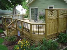 a wooden deck in front of a house with an umbrella and flowers on the ground