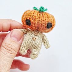 someone is holding a tiny knitted doll in their left hand and it looks like an orange pumpkin