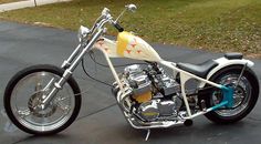 a white and yellow motorcycle parked on top of a driveway next to a grass covered field