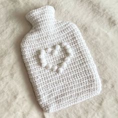 a crocheted white bottle with hearts on the top is laying on a bed