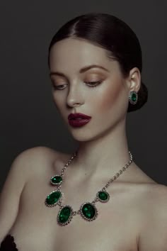 a woman wearing a necklace with green stones on her chest and red lipstick in the foreground