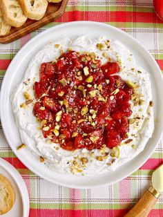 a bowl of whipped cream topped with fruit and nuts on a plaid tablecloth next to pretzels