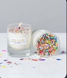 a candle with sprinkles sitting next to a glass container filled with confetti