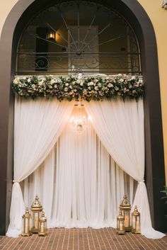 Ceremony backdrop with draping, lanterns, a chandelier and a floral beam. Wedding Draping Backdrop Ceremony Arch, White Drapes Wedding Ceremony Backdrop, Draped Photo Backdrop, Backdrop With Chandelier, Ring Ceremony Backdrop, Backdrop With Drapes, Backdrop With Curtains, Backdrop Draping Ideas, Roka Ceremony Decoration