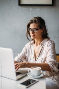 a woman sitting at a table with a laptop computer in front of her and a cup of coffee