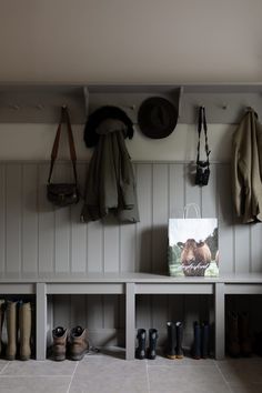 several coats and boots are hanging on the wall next to a coat rack with hats