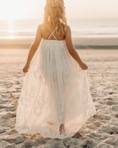 a woman in a white dress is walking on the sand at the beach with her back to the camera