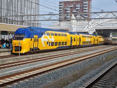 a yellow and blue train traveling down tracks next to a tall building with lots of windows