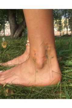 a person standing in the grass with their bare feet and flowers on her foot,