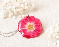 a pink flower is sitting on a white surface with flowers around it and a silver chain