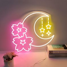 a neon sign that is next to a book and some flowers in a vase on a table