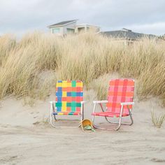 two lawn chairs sitting on top of a sandy beach next to tall grass and sand dunes