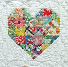 a patchwork heart made up of many different colors and patterns on a white quilt