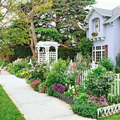 a house with many flowers in front of it and a white picket fence around the yard