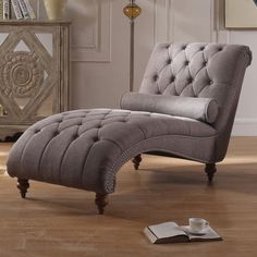 a gray chaise lounge chair sitting on top of a hard wood floor next to a book