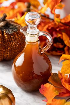 a bottle of syrup sitting on top of a table next to pumpkins and leaves