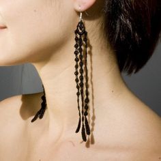 a close up of a woman wearing earrings with long black beads on her back neck