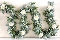 white flowers and greenery are arranged in the shape of the letter e on a wall