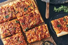 several square pizzas are sitting on top of a cutting board next to a knife