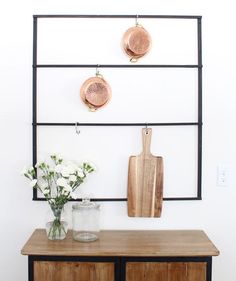 a wooden table topped with two vases filled with white flowers next to a cutting board