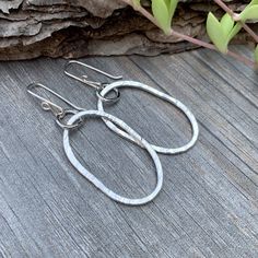 Embrace the charm of rustic elegance with our Riverstone Sterling Silver Dangle Earrings. Handcrafted to showcase the natural beauty of a riverstone shape, these large, oval earrings bring a playful imperfection that adds a casual yet sophisticated touch to any look. Made from sterling silver, they’re perfect for everyday wear, adding an artisanal flair to both casual and bohemian styles. Thoughtfully designed, these earrings are an ideal choice for those who appreciate unique, timeless accessor Nickel-free Oval Teardrop Earrings, Nickel Free Oval Minimalist Earrings, Nickel-free Oval Minimalist Earrings, Minimalist Nickel-free Oval Earrings, Rustic Silver Oval Jewelry, Minimalist Oval Metal Earrings, Handmade Rustic Oval Jewelry, Hand Forged Oval Artisan Earrings, Artisan Oval Hand Forged Earrings