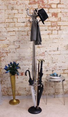 an umbrella and hat stand in front of a brick wall with a flower pot on it