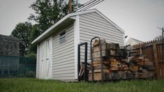 a pile of wood sitting in front of a white shed on top of a lush green field