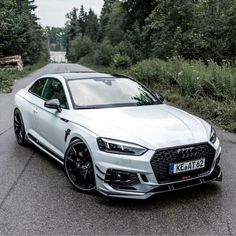 a white car parked on the side of a road next to some bushes and trees