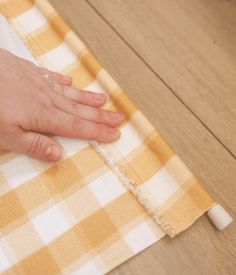 a person's hand on a yellow and white checkered tablecloth with a wooden floor in the background